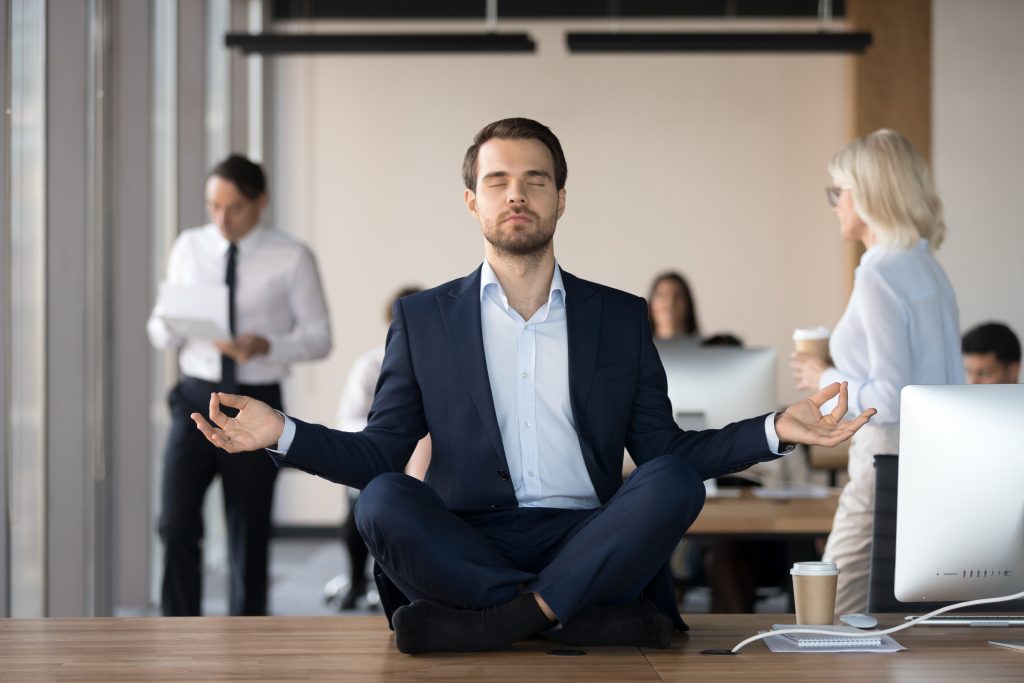 Homme d'affaires assis sur son bureau en position du lotus les yeux fermés