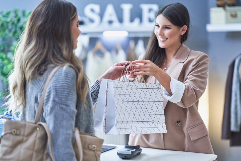 Une vendeuse tend un sac de produits à une autre femme qui vient de les acheter après avoir reçu une communication de proximité
